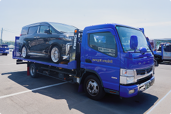 黒いミニバンを積載した青い車両運搬トラック